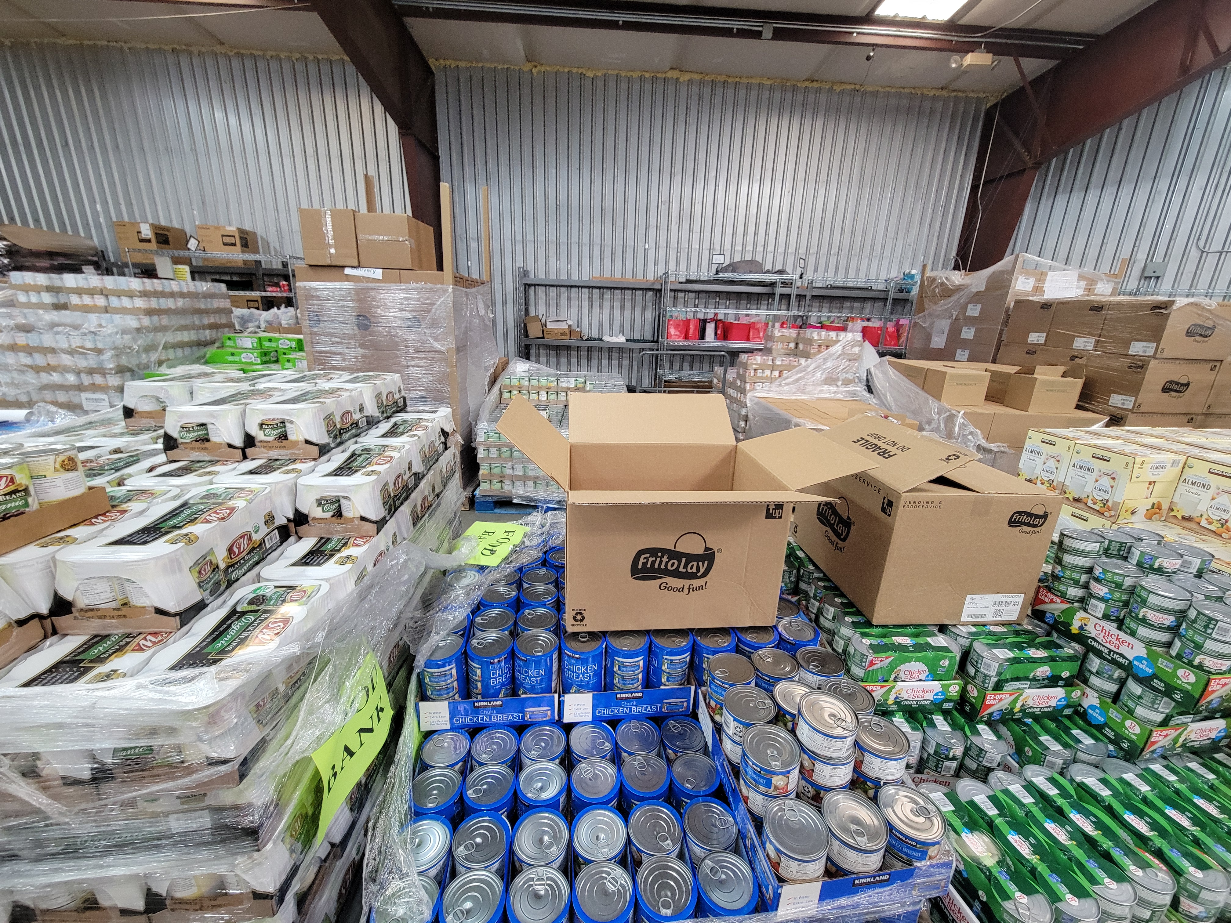 Warehouse area with pallets of canned goods, shelves full of stuff, and cardboard boxes.